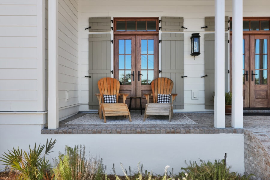 Cozy front porch with Adirondack chairs and a black and white checkered pillow, featuring wooden double doors and charming exterior details of a modern home.