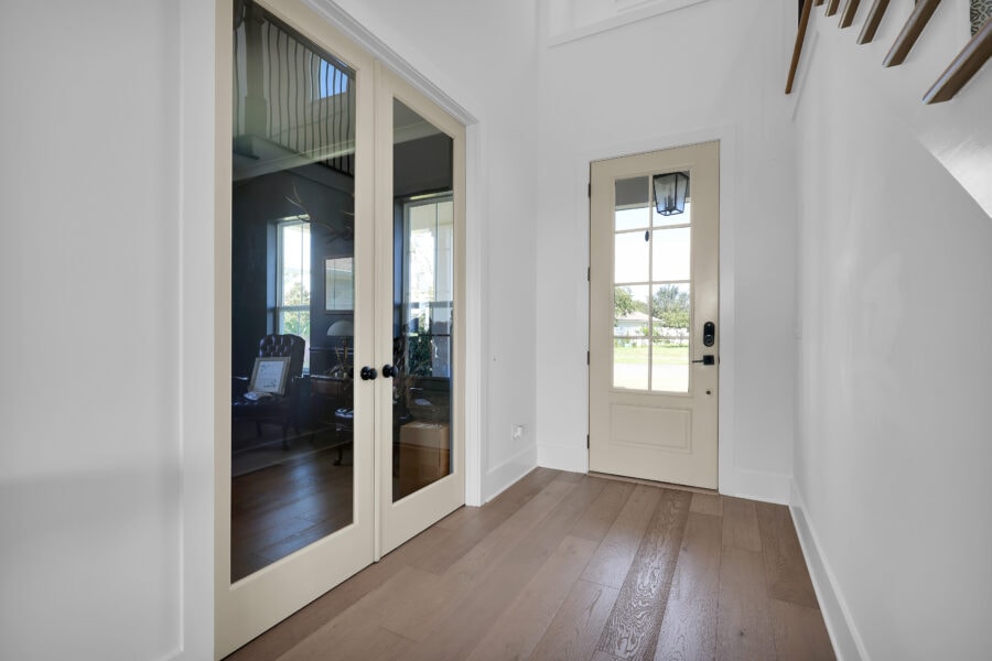 Modern entryway with glass-paneled double doors and a front door with a large window, featuring natural light, white walls, and light wood flooring, creating a welcoming and airy atmosphere.