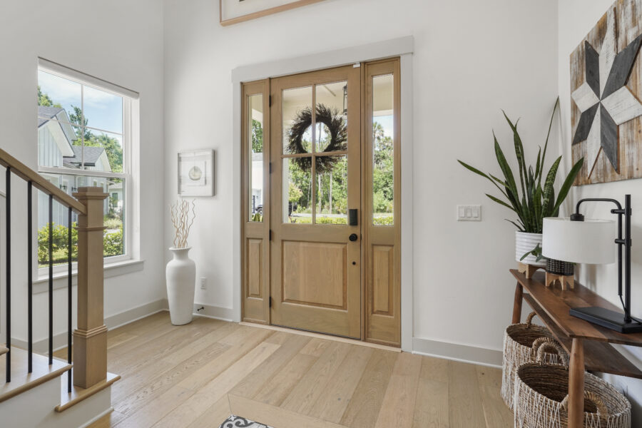 Warm wood front door with glass panes, leading into a bright and welcoming home entryway with natural light, modern decor, and greenery visible outside.