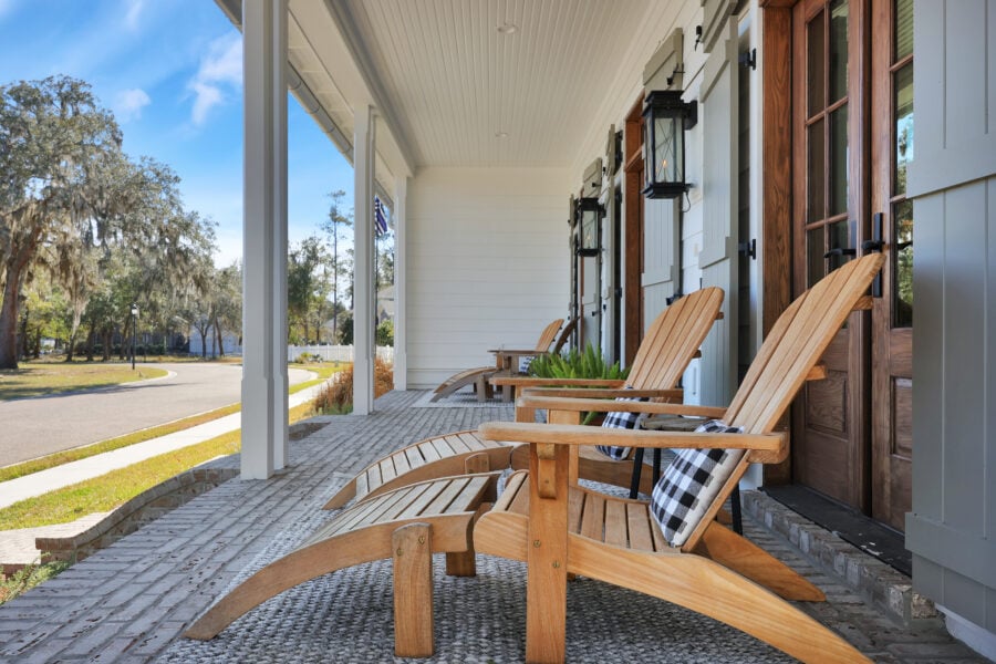 Cozy front porch with three Adirondack chairs, potted plants, and wooden shutters, showcasing a welcoming outdoor space on a sunny day in a suburban neighborhood.