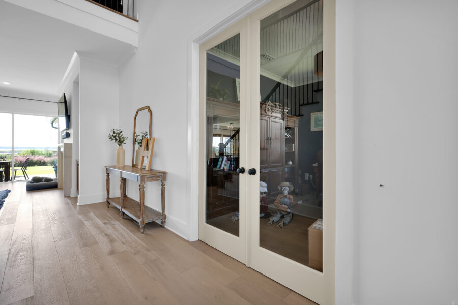 Modern interior entryway with white walls, wooden floor, glass double doors leading to a cozy room, and decorative accents likeVases with greenery on a wooden console table.