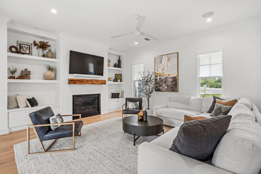Modern living room with white walls, a cozy white sectional sofa, black accent chair, built-in shelves, a fireplace with a wooden mantle, a large wall-mounted TV, and stylish decor in a bright, airy space.