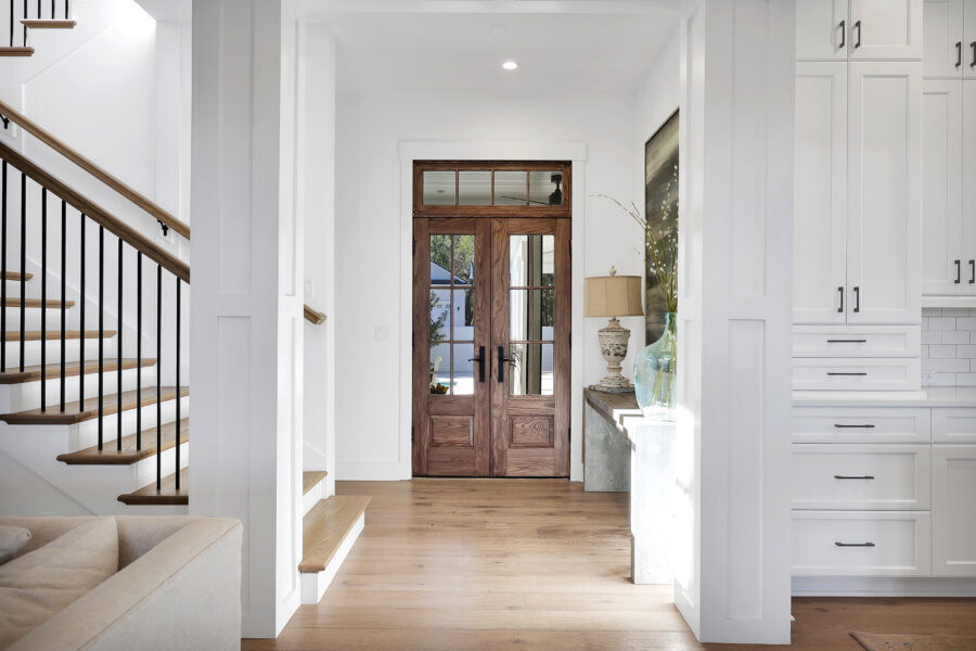 Warm wooden front door with glass panes in a modern home's entryway, featuring white walls, brass accents, and minimalist decor for a stylish and welcoming interior.