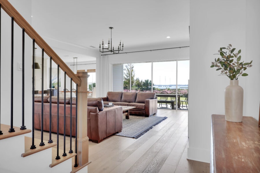 Modern living room with large windows showing scenic outdoor views, featuring leather sofas, hardwood flooring, contemporary chandelier, and minimalist decor enhancing natural light and spaciousness.