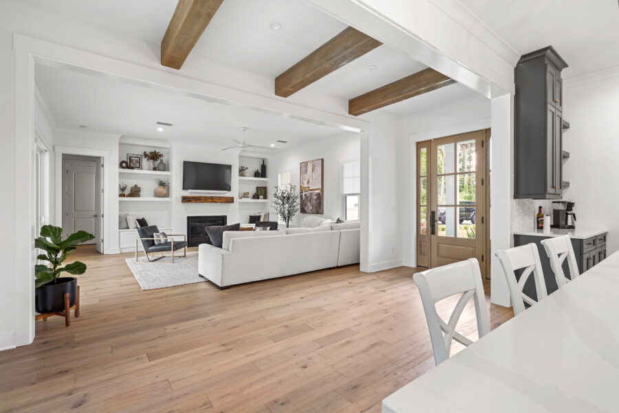 Modern living room with white walls, hardwood flooring, a cozy fireplace, and a flat-screen TV, featuring stylish built-in shelving and large windows that let in natural light.