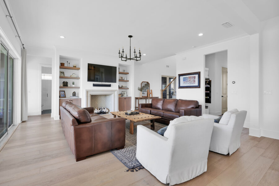 Modern living room with white walls, light wood flooring, brown leather sofas, white armchairs, a fireplace with built-in shelves, flat-screen TV, and contemporary decor.