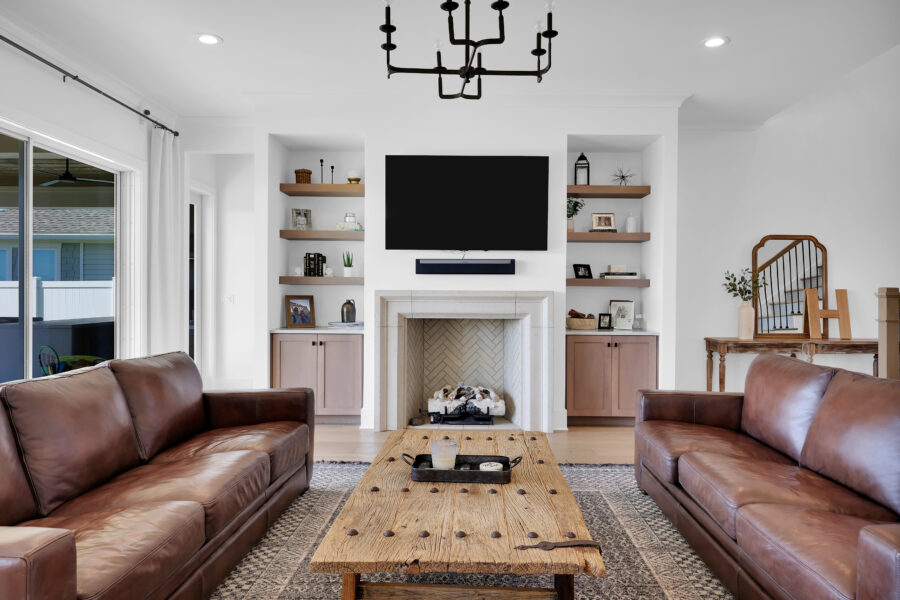 Modern living room with white walls, a fireplace, built-in shelves, leather sofas, and a large flat-screen TV, showcasing stylish interior design and contemporary decor.