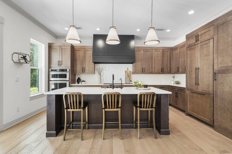 Modern kitchen with a large island, wooden cabinets, black hood vent, and pendant lighting, designed by John Merrill Homes.