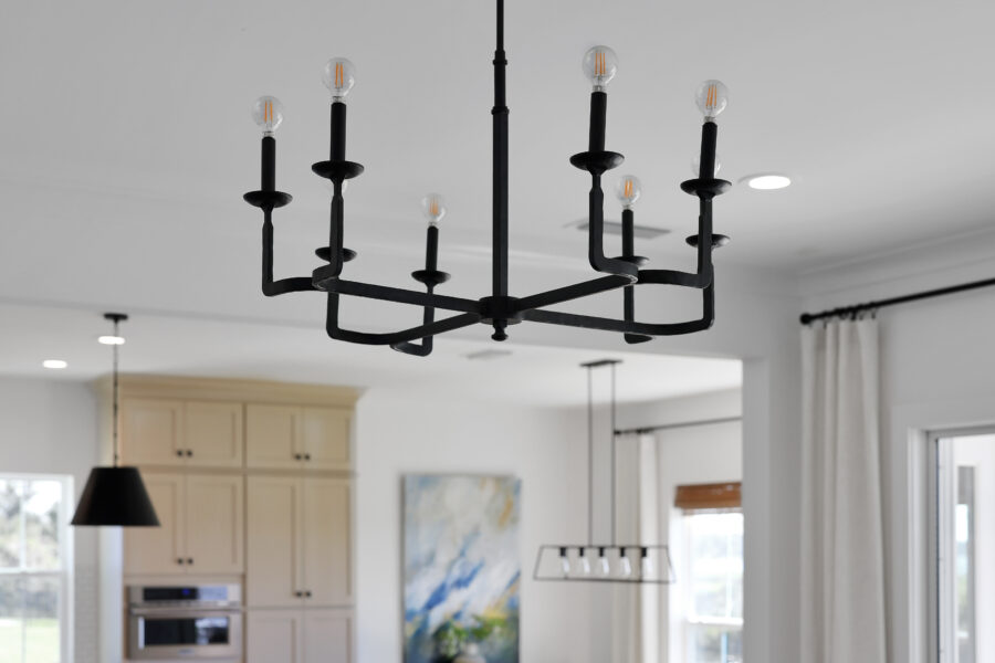 Modern black chandelier with exposed bulbs hanging in a bright, open-concept kitchen and dining area.