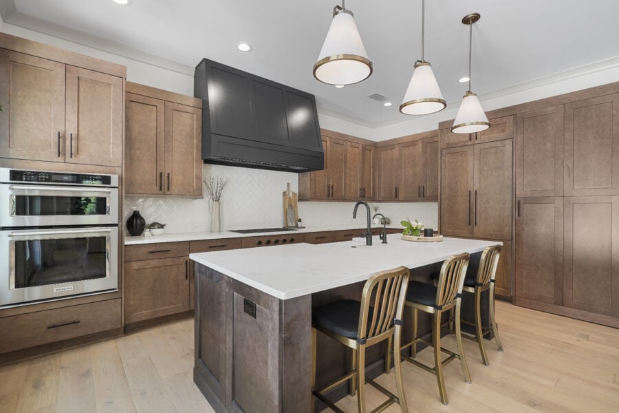 Bright modern kitchen featuring wooden cabinetry, a large central island with white marble countertop, black fixtures, contemporary pendant lights, and stainless steel appliances.