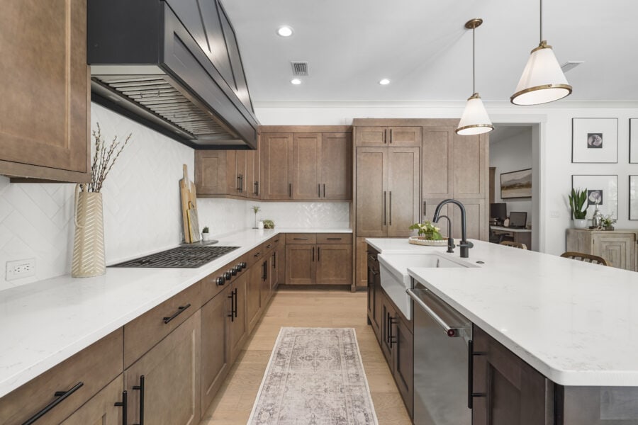 Modern kitchen with wood cabinets, white marble countertops, black hardware, pendant lighting, and a farmhouse sink, showcasing a stylish and functional space for cooking and entertaining.