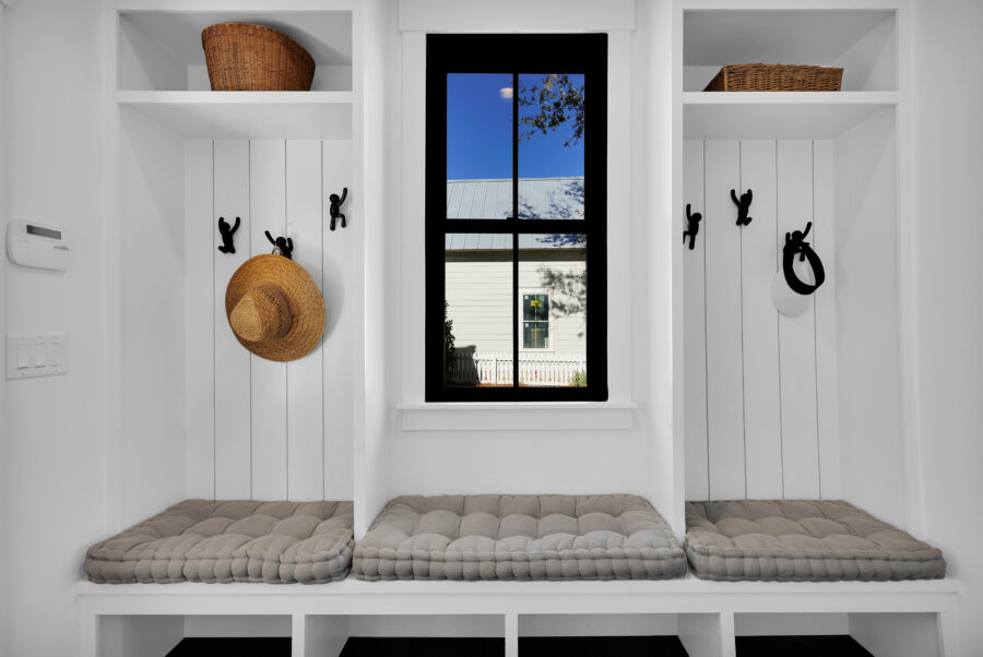 Cozy built-in mudroom with white shiplap walls, a window with view of the outdoors, storage cubbies with cushions, and hooks for hats and accessories, designed for organization and comfort.