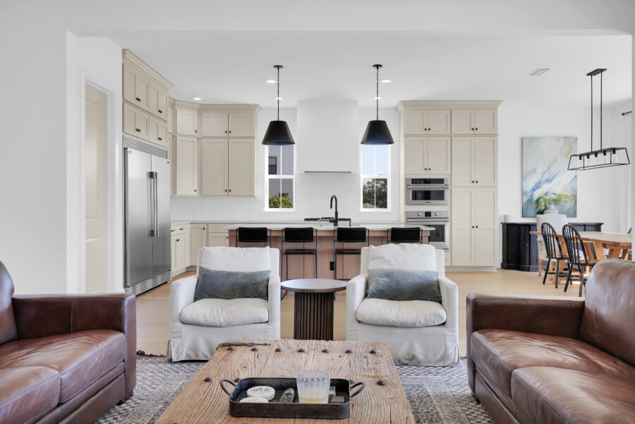 Modern open-concept kitchen and living room featuring neutral tones, stylish lighting, and contemporary furniture in a new home by John Merrill Homes.