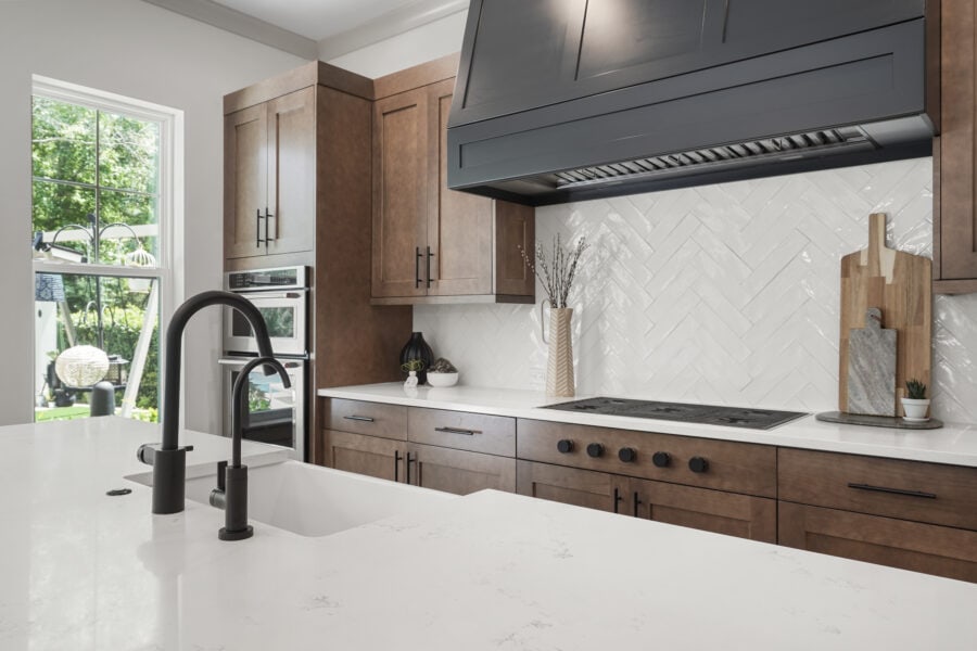Bright modern kitchen with white quartz countertops, dark wood cabinets, and a white herringbone tile backsplash, featuring a black stove and a large window bringing in natural light.