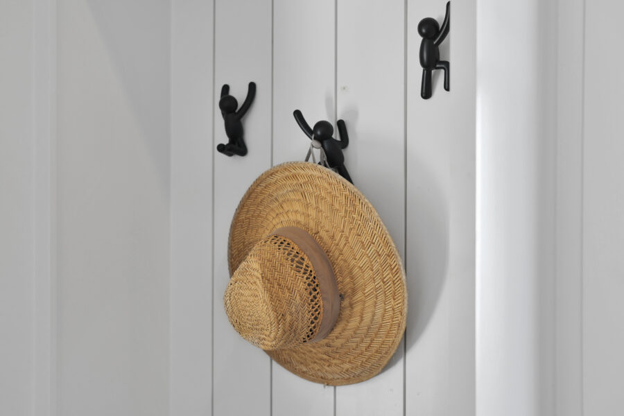 Straw hat hanging on black hooks on a white wooden wall in a modern home entryway.