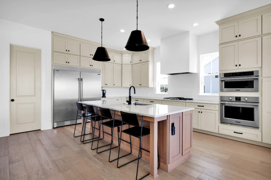 Modern kitchen with white cabinetry, marble island counter, black pendant lights, stainless steel appliances, and hardwood flooring. A bright and spacious setting perfect for cooking and entertaining.