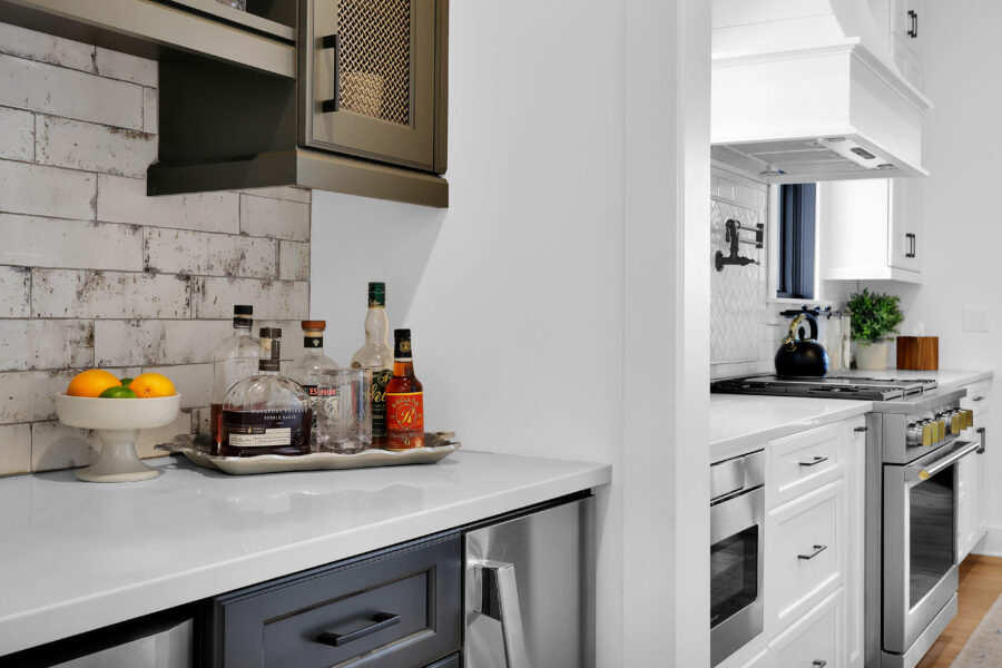 Spacious modern kitchen featuring white cabinetry, stainless steel appliances, black faucet, and a backsplash with a white herringbone tile pattern, complemented by a small window and green plant.