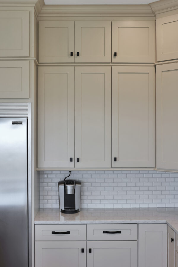 Luxury kitchen with white cabinetry, marble countertop, tiled backsplash, and a modern coffee maker for a stylish and functional culinary space.