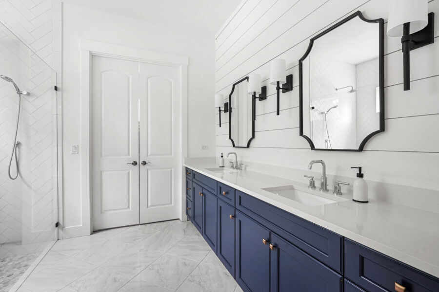 Contemporary bathroom vanity with white countertops, navy-blue cabinets, black-framed mirrors, and modern black wall sconces. Features dual sinks, sleek fixtures, and a spacious design for elegance and functionality.