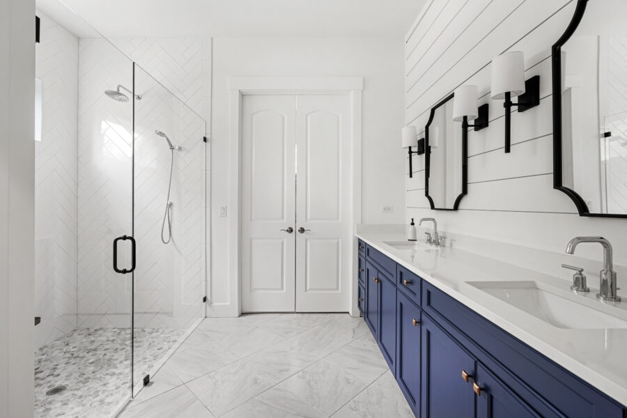 Luxurious modern bathroom featuring a sleek double vanity with navy blue cabinetry, contemporary fixtures, and a spacious walk-in shower with white tiles and pebble flooring, showcasing elegant design and quality craftsmanship.