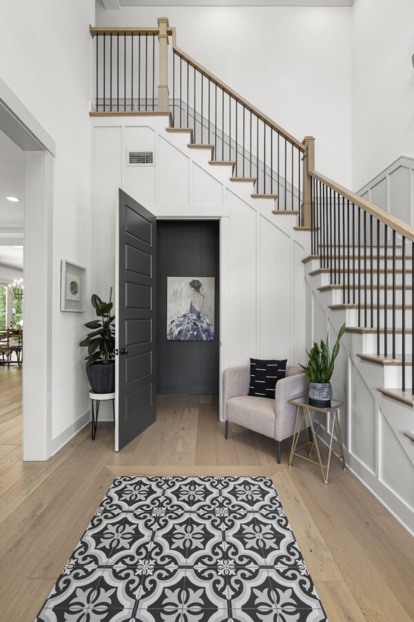 Modern entryway with black and white decor, cozy armchair, indoor plants, and a stylish stairway with black metal railing and wooden handrail at John Merrill Homes.