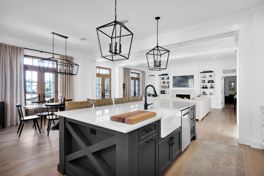 Bright open-concept kitchen with white countertops, black cabinets, and modern black pendant lighting, overlooking a cozy living room with a fireplace and built-in shelves, perfect for family gatherings.