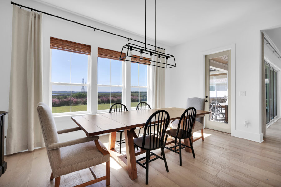 Modern dining room with large windows, light-colored hardwood floors, and a wooden dining table surrounded by a mix of upholstered and wooden chairs, offering a bright and airy atmosphere.