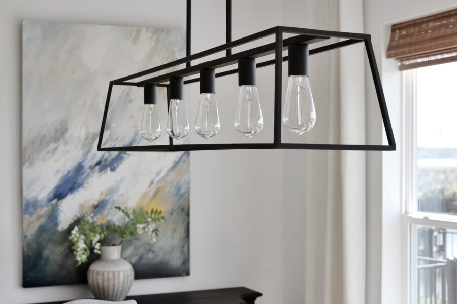 Modern black-framed pendant light fixture with exposed bulbs hanging in a contemporary living space.