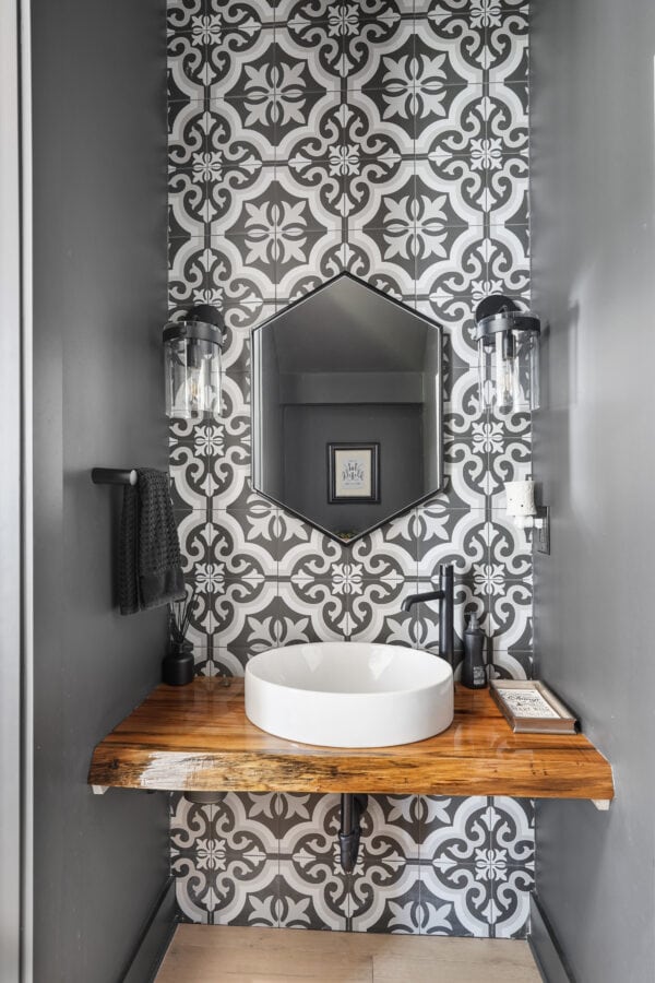 Contemporary bathroom vanity with a round vessel sink, black fixtures, and chic geometric black-and-white tile wall. Modern black wall sconces illuminate the space.