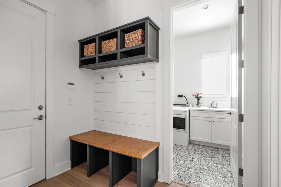 Modern laundry room with white cabinetry, natural wood and black accent storage, and a decorative tile floor, showcasing stylish design and functionality.