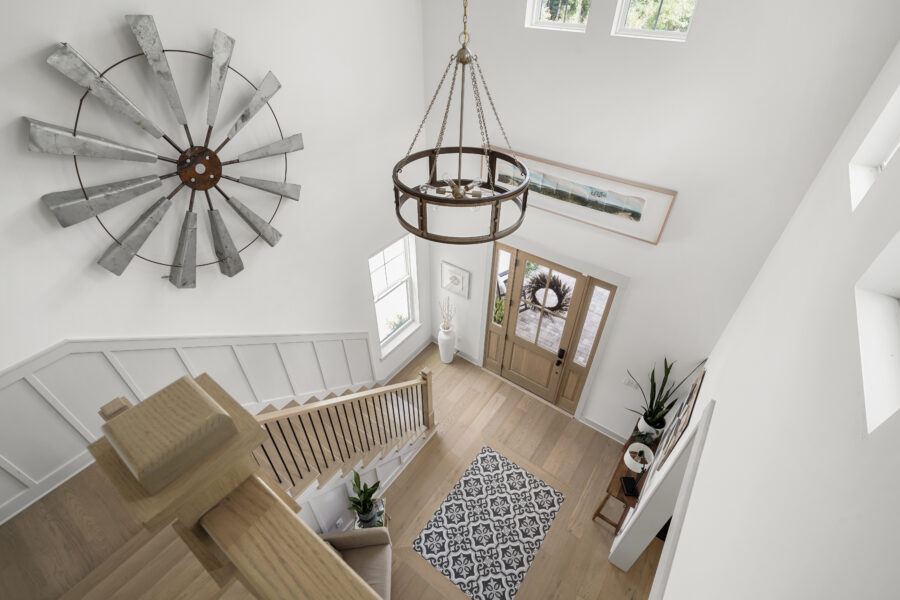 Rustic windmill wall art and a brass chandelier hang in a bright, modern foyer with natural light, wooden flooring, and minimalist decor, creating a welcoming entrance.