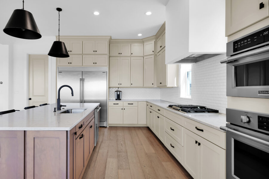 Modern kitchen with white cabinetry, stainless steel appliances, a central island with a black faucet, and warm wood flooring, designed for functional and stylish living.