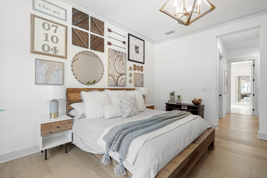 Modern bedroom with a stylish gallery wall featuring framed artwork, mirrors, and decorative pieces. The room includes a cozy bed with plush pillows and a textured throw, accented by natural wood furniture and light-colored walls.