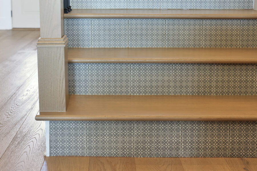 Stylish wooden staircase with decorative black and white patterned tile risers and light hardwood treads. Modern interior design features a mix of textures and patterns.