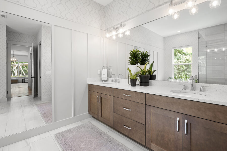 Modern bathroom with a double vanity, white speckled countertop, and stylish wooden cabinets, featuring indoor plants, a large mirror, and ample natural light from a window, creating a bright and inviting space.