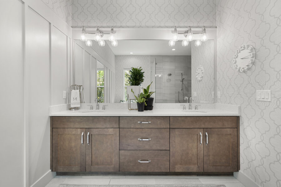Elegant bathroom vanity with dual sinks, wooden cabinetry, a large mirror, decorative plants, modern light fixtures, and a spacious walk-in shower in a contemporary home interior.