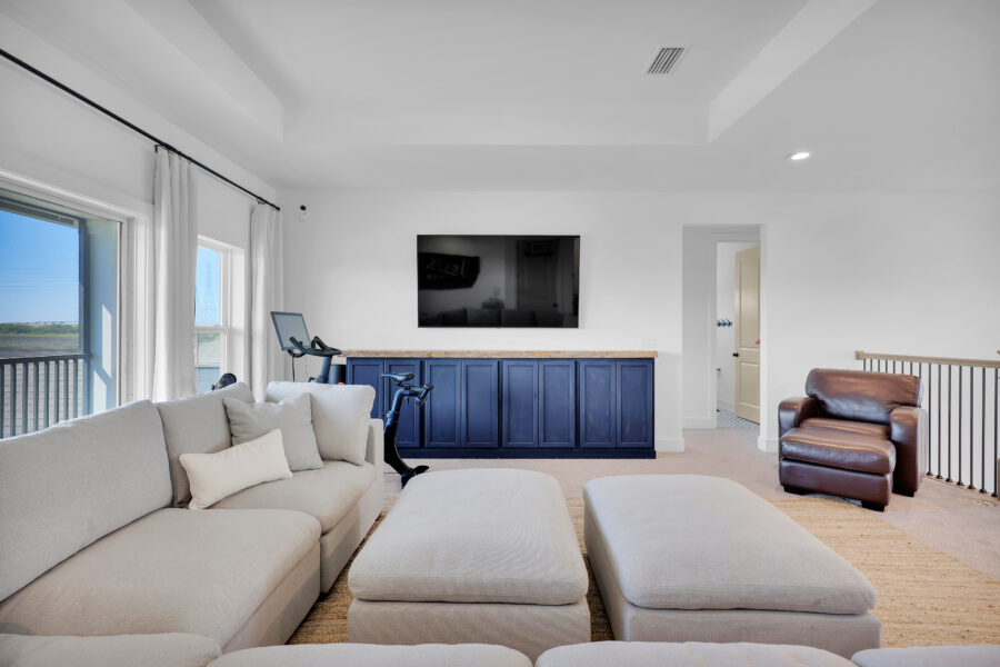 Spacious living room featuring large windows, white walls, a white sectional sofa, a brown leather armchair, a wall-mounted TV, and a built-in blue cabinet with a marble countertop, offering a bright and modern interior design.