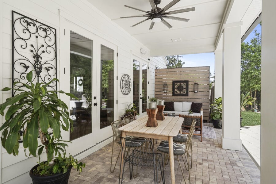 Modern outdoor covered patio with dining table, lounge seating, greenery, and decorative wall accents, featuring white siding and glass doors, ideal for relaxing and entertaining.