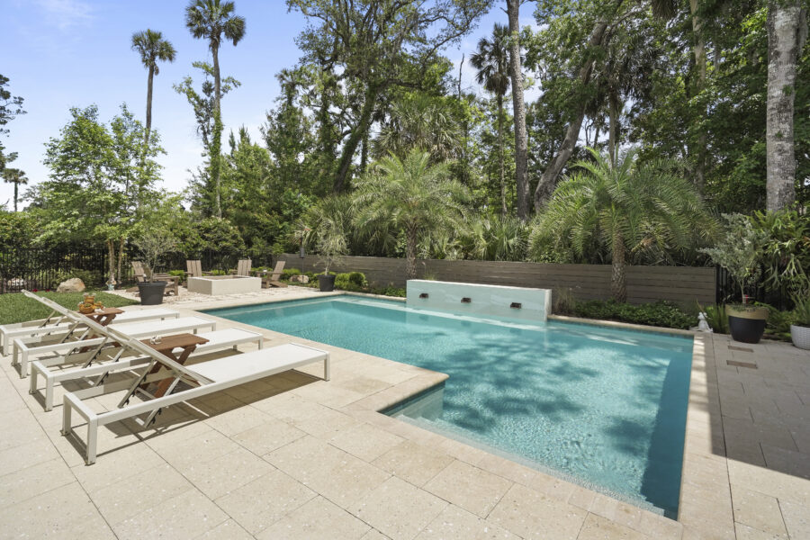 Modern backyard swimming pool surrounded by lush tropical trees and outdoor furniture, creating a relaxing and luxurious outdoor living space.