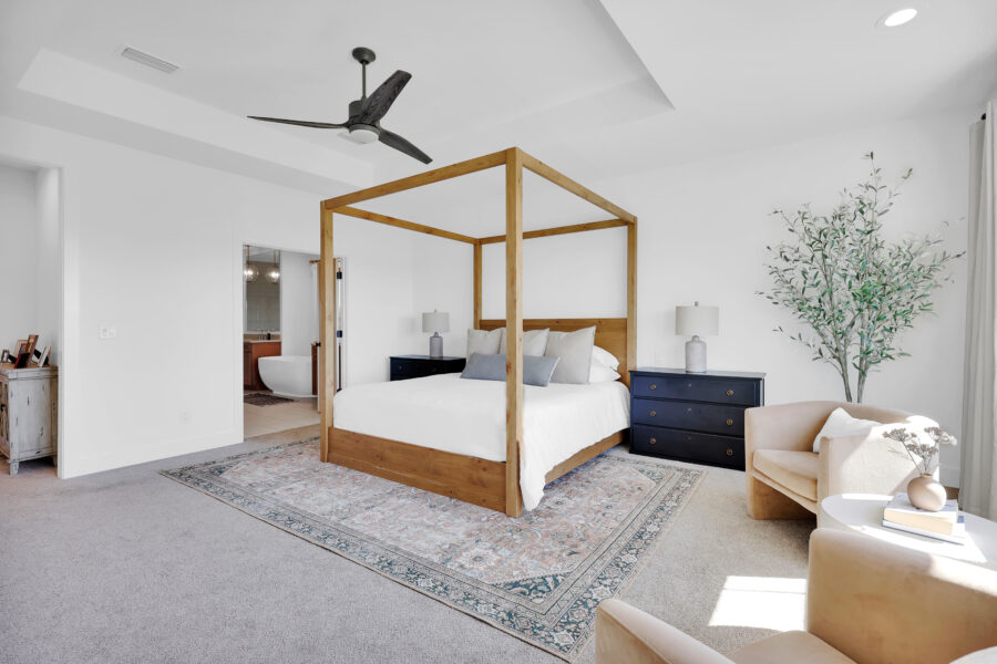 Bright modern bedroom with a four-poster bed, navy nightstands, and a cozy armchair by a window, featuring a decorative rug and contemporary decor for stylish living.