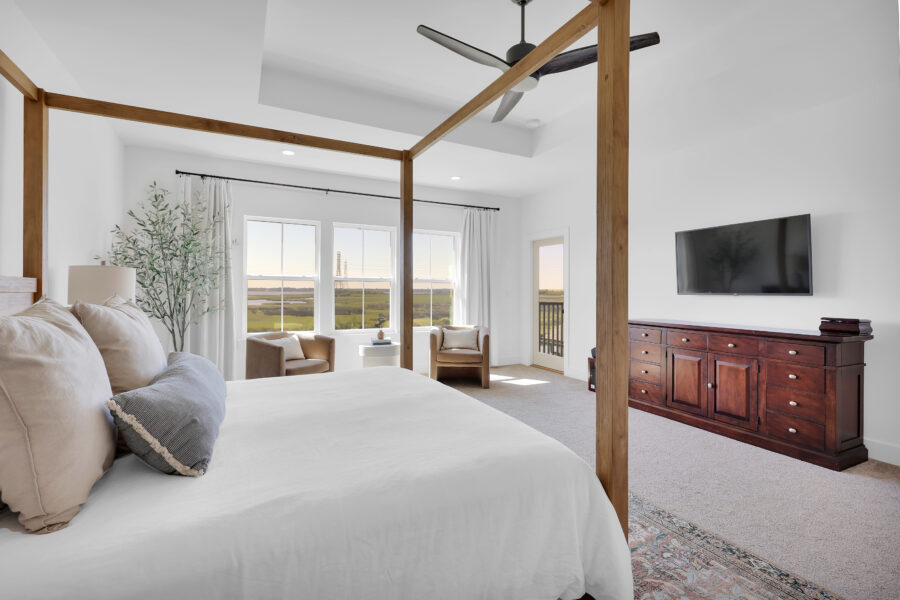 Modern master bedroom with large windows, cozy seating area, ceiling fan, and elegant furniture, showcasing a relaxing and stylish space in a new home by John Merrill Homes.