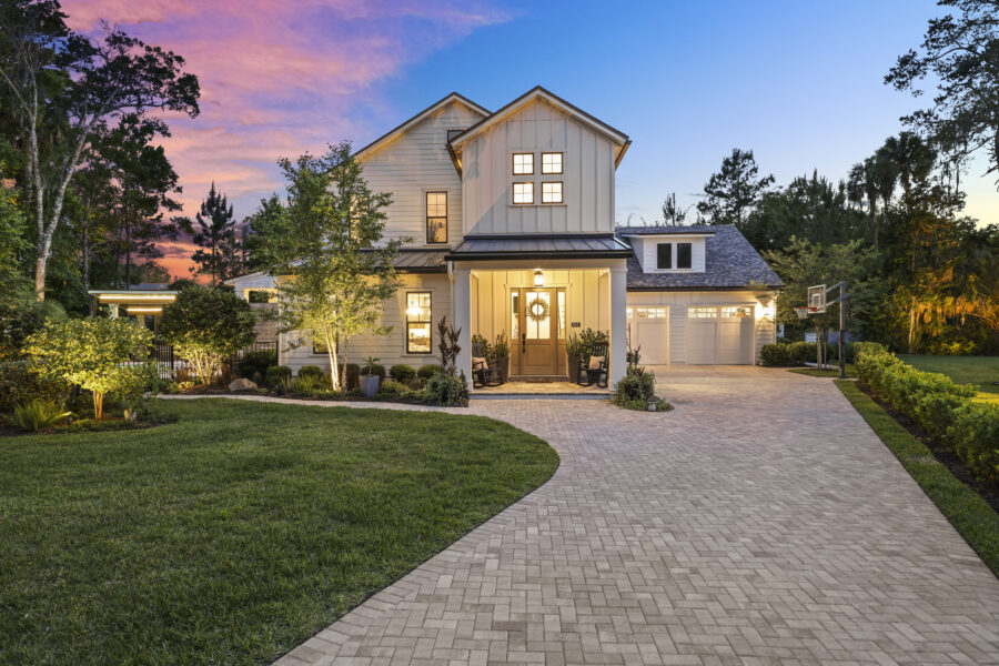 Luxurious modern farmhouse style home with white exterior, large front porch, landscaped yard, and illuminated windows at dusk, showcasing elegant architecture and inviting curb appeal.