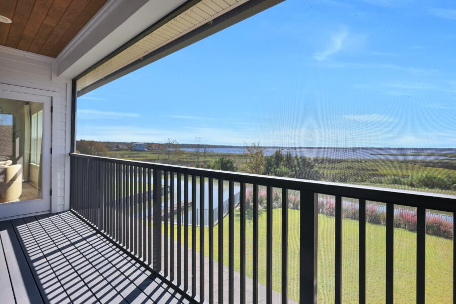 Expansive balcony overlooking a scenic landscape with water, greenery, and a clear blue sky, providing a peaceful outdoor space connected to a modern home.