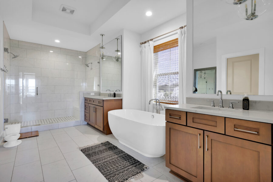 Spacious modern bathroom featuring a walk-in shower, freestanding bathtub, wooden vanities with marble countertops, and large windows providing natural light.