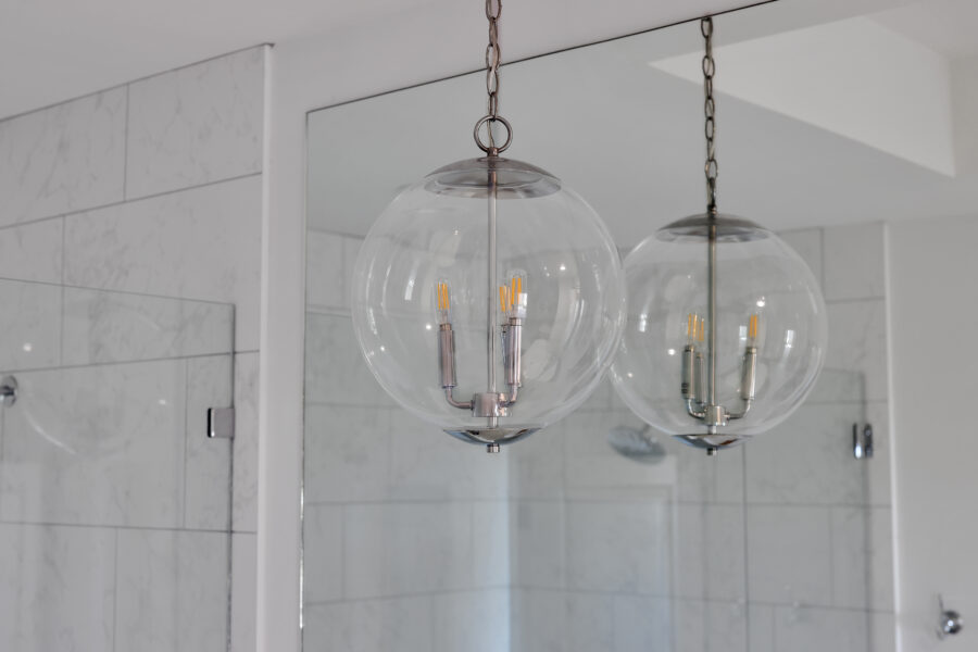 Modern glass pendant lights with metallic accents hanging in a bright bathroom, reflected in a large mirror, creating a sleek and contemporary aesthetic.
