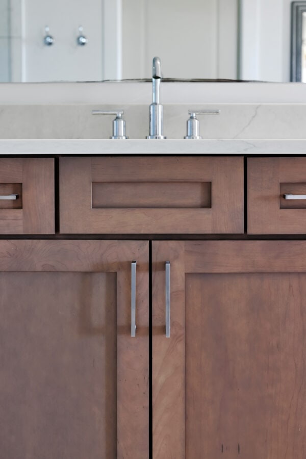 Modern kitchen vanity with wooden cabinets and stainless steel handles, featuring a marble countertop and a chrome faucet, in a newly built home by John Merrill Homes.