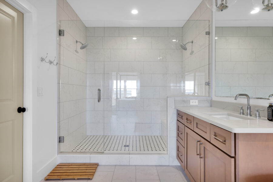 Modern bathroom featuring a spacious walk-in shower with glass enclosure, white marble tiles, and a sleek wooden vanity with double sinks. Bright, clean design perfect for contemporary home living.