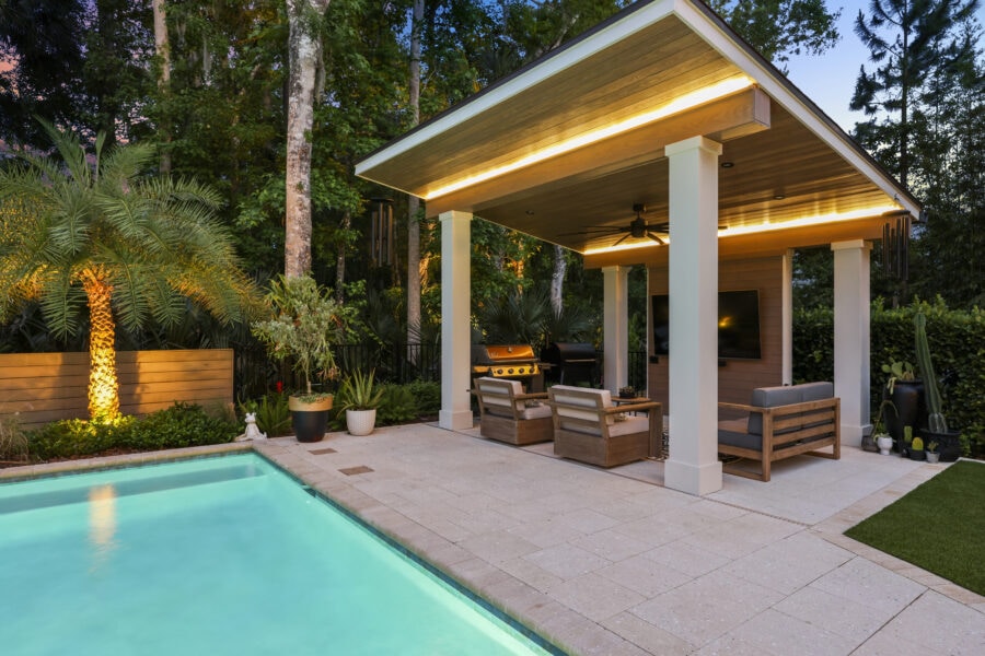 Modern backyard with a swimming pool, outdoor lounge area, and lush greenery, perfect for relaxation and entertaining at John Merrill Homes.