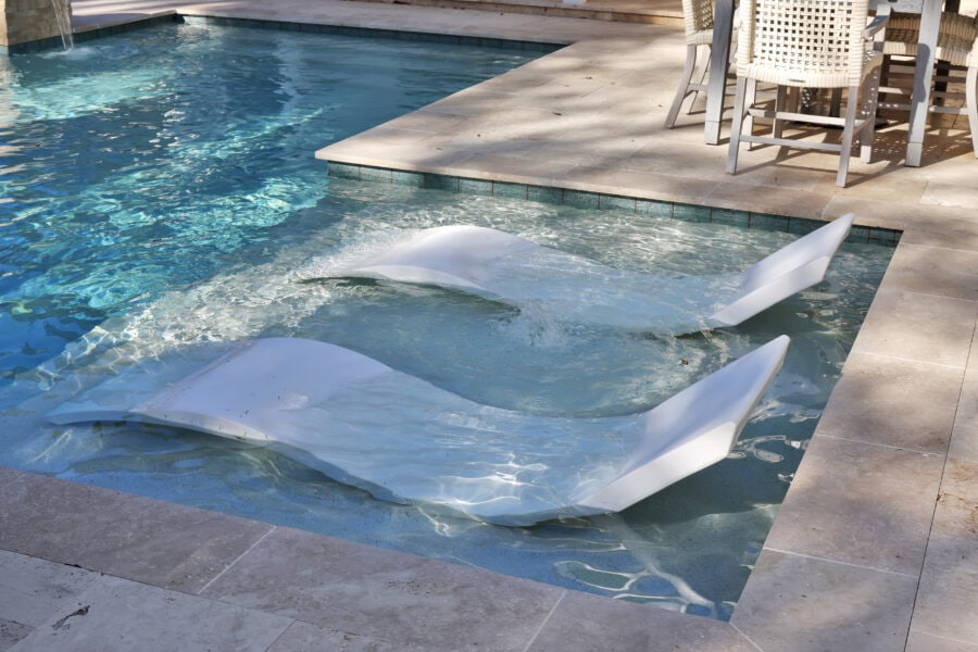 Floating modern pool chairs and outdoor dining area at luxury home poolside pool deck.