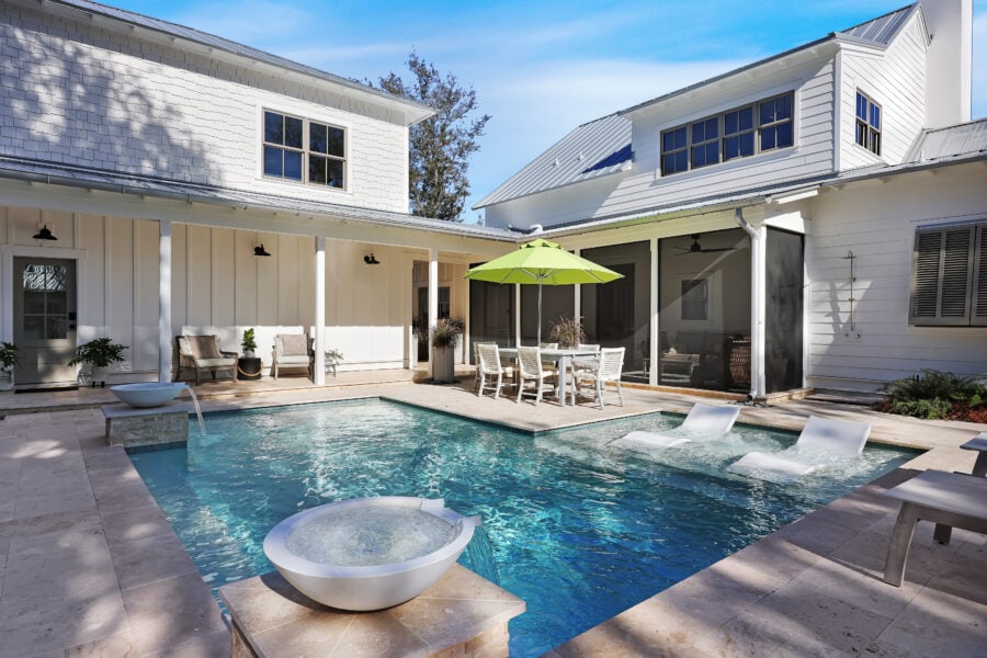 Modern white house with a backyard pool, outdoor seating area, and shaded dining space, showcasing elegant poolside design and contemporary architecture.